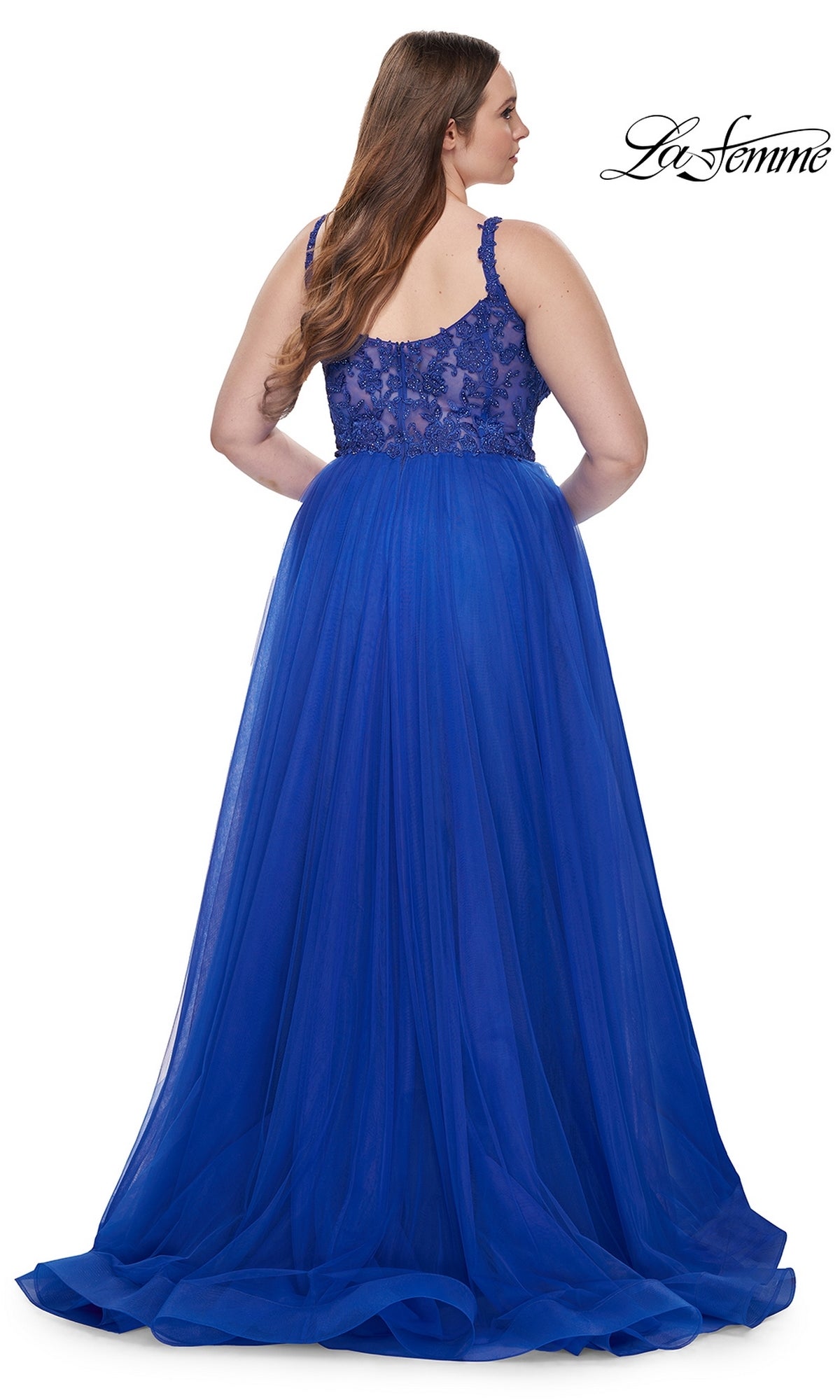 A woman is shown from the back wearing the La Femme Long Prom Dress 31394, a floor-length royal blue gown with an embroidered lace bodice, tulle skirt, thick lace straps, and a fitted waist—an elegant plus-size prom choice.